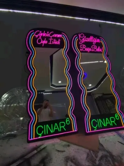 Pembe ve mavi neon çerçeveli iki dalgalı ayna, alt köşelerinde yeşil logo yazısı