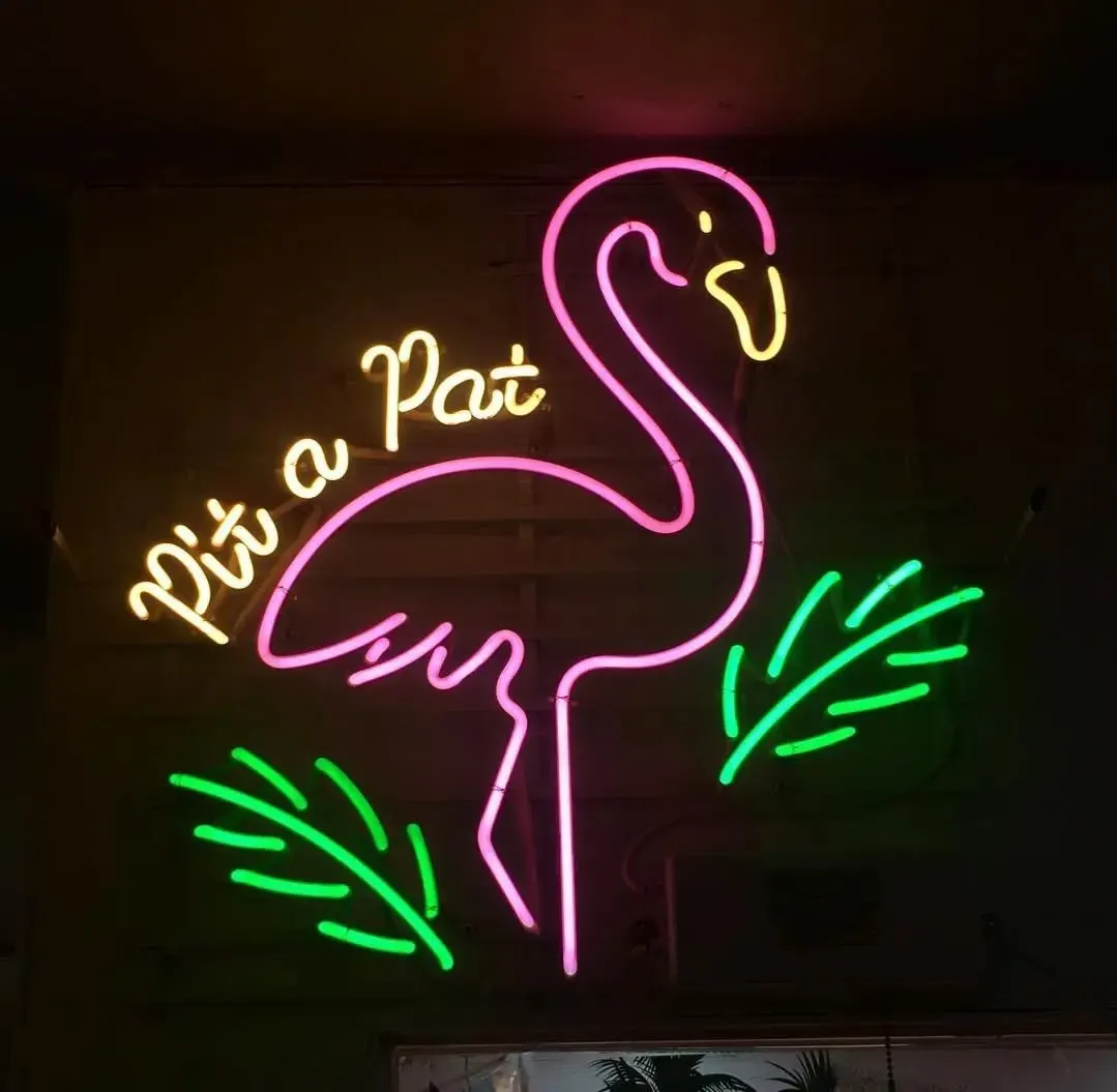 Pembe flamingo, yeşil yapraklar ve sarı yazılı neon