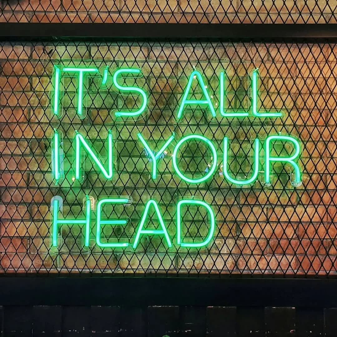 Tel ızgara üzerinde yeşil büyük harflerle 'It's all in your head' neonu